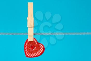 	red decorative heart hung on clothesline. isolated on blue background