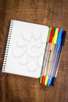 Spiral notebook and colorful pens on the wooden desk 