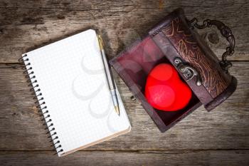  Red heart in the  box and notebook with pen on wooden floor