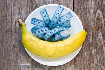 Healthy eating concept. Banana and measurement tape in a plate.