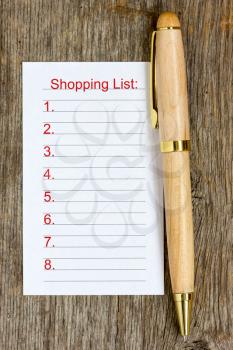 Pen and shopping list on wooden background 