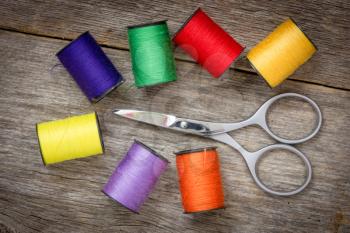 Scissors and spools of colored thread on the wood background