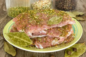 Raw pork with spices in a plate on wooden background