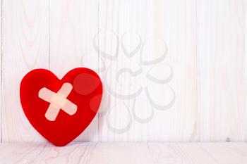 Injured heart with plaster on the wooden background
