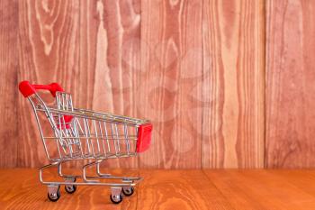 Empty mini shopping cart against brown wooden background