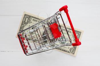 Shopping cart and dollar on the white wooden surface