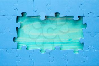 Blue jigsaw puzzle pieces arranged as a border around a green wooden surface  