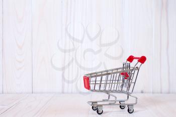 Empty mini shopping cart against white wooden background