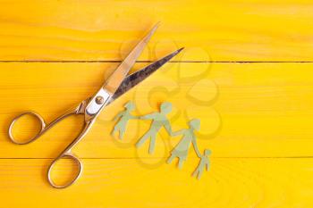 Scissors and  paper cut people on the yellow wooden surface