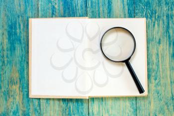 Open book and magnifier on blue wood surface