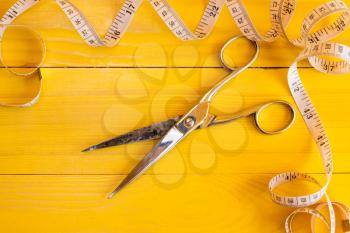Metal scissors and measure tape on yellow background. Fashion industry concept.