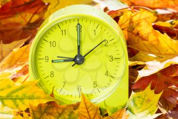 Alarm clock on autumn leaves. Time change concept. In autumn we change clock one hour back.
