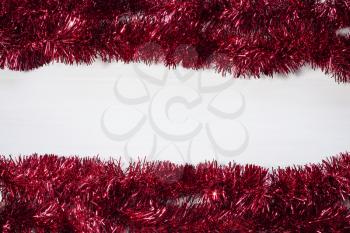 Christmas frame from red tinsel on white wooden background