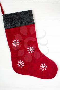 Red Christmas sock with snowflakes for Santa gifts hanging on wooden background. 