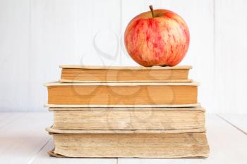Stack of books with red apple on white wooden background