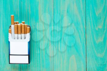 Open pack of cigarettes on blue wooden background with copy-space