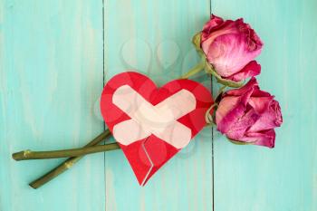 Injured heart and old roses on blue wooden background