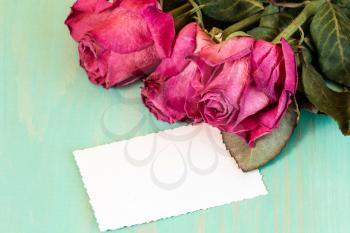Dry roses bouquet and blank greeting card over wooden table