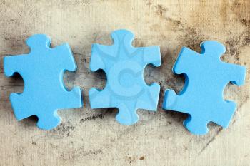 Three blue puzzle pieces on old canvas background