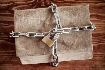 Old book with chain and padlock on wooden table