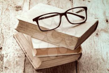 Old books and reading glasses on the wooden background