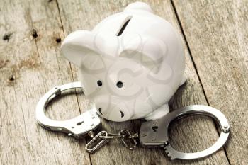 Piggy bank with handcuffs on old wooden background