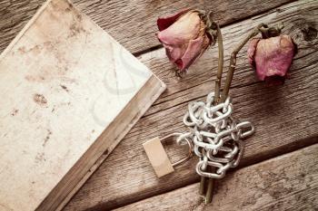 Old book and two dry chained roses on the wooden background