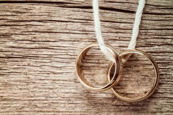 Wedding rings hanging on rope over wooden background. Vintage image.