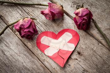 Broken paper heart and old roses on wooden background