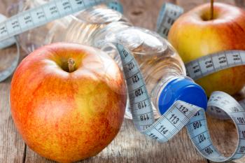 Bottle of water, measuring tape and fresh  apples on the wooden background