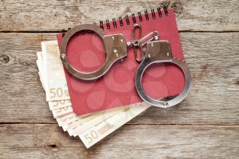 Handcuffs on notebook with euro banknotes. Bribery concept.