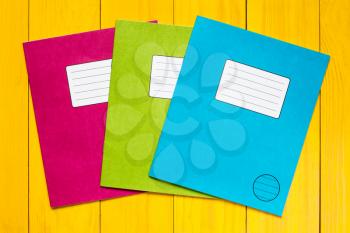 Three colored exercise books on the yellow wooden background