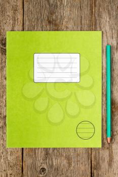 Green exercise book and pencil on wooden background