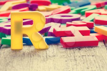 Capital letter R in a front of other colorful plastic letters. Vintage filter.