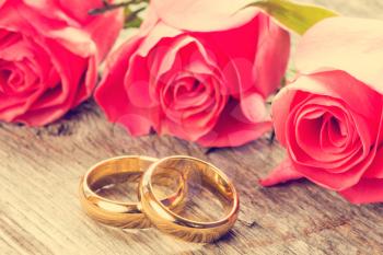 Wedding rings with pink roses on wooden background