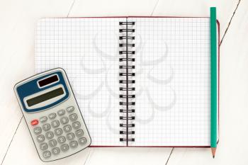 Electronic calculator and spiral notebook on the white wooden background