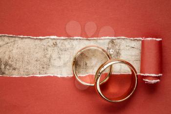 Torn red paper and two gold wedding rings