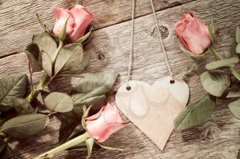  Blank heart shaped tag and three roses on wooden background.