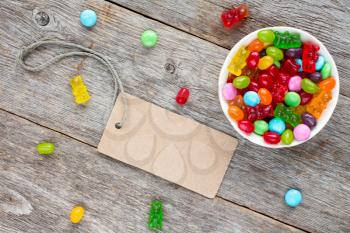 Blank tag and bowl with mixed candies on wooden background