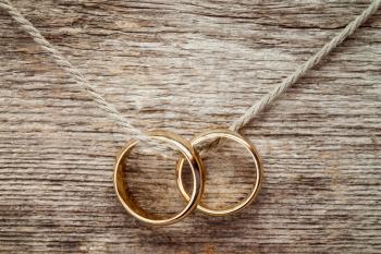Wedding rings hanging on rope over wooden background. 
