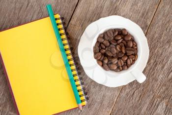  Blank notebook and  cup with roasted coffee beans on wooden background. Top view image.
