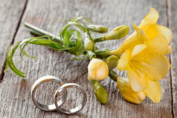 Wedding rings with freesia flower on wooden background