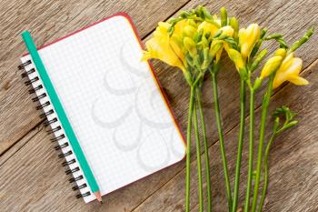 Yellow freesia flowers and blank notebook on wooden background