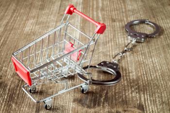  Shopping cart and handcuffs on old wooden background