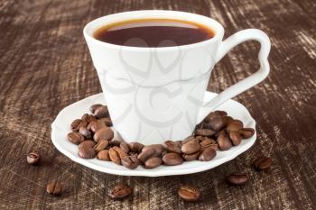   White coffee cup with roasted coffee beans on wooden background. 