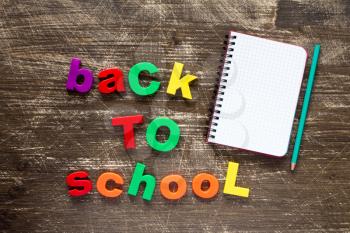 Sentence Back to school in colorful plastic letters and blank notebook over dark wooden background