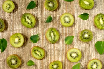 Sliced kiwi fruit and green leaves on wooden background 