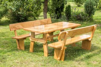 Wooden set of table, benches with backrests on green grass lawn. Vacation place in garden. Summer leisure time.