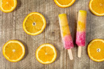  Popsicles with sliced orange fruit on wooden background. Top-view.