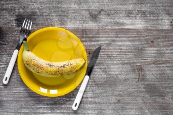 Fork,knife and yellow plate with banana on wooden background.Top view,copy-space.